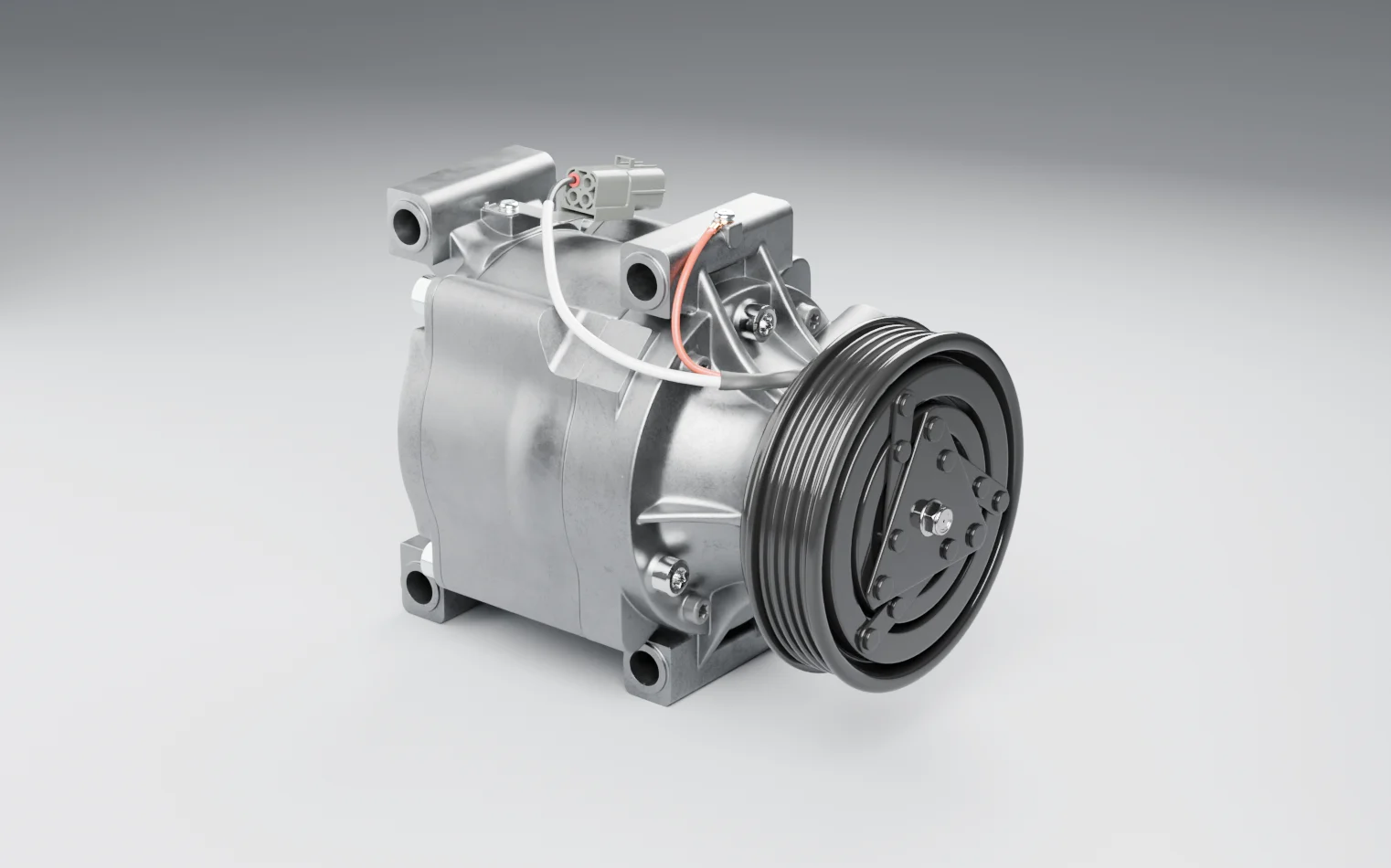 A belt-driven automotive air-conditioning compressor on a grey studio floor: the grooved pulley and clutch plate at the front, the clutch connector and its two leads on top