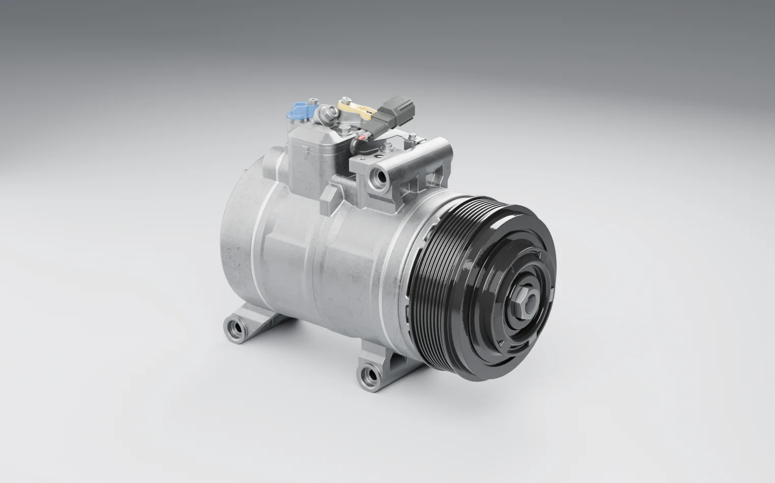 A belt-driven air-conditioning compressor on a grey studio floor: a multi-groove pulley with a centre nut, capped fittings and a connector on top